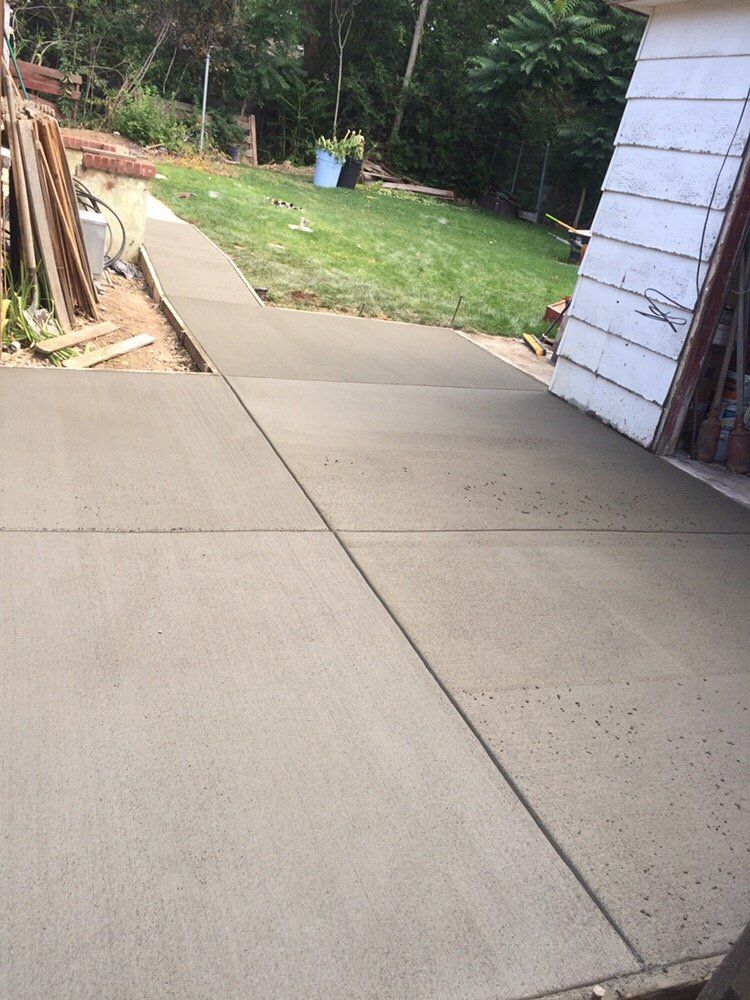 Concrete driveway leading to a grassy yard, with a white brick wall and stacked wood on the left