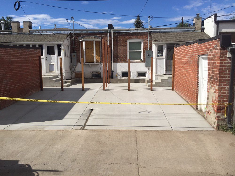 Residential driveway blocked by yellow caution tape, with brick buildings and a concrete lot behind it.