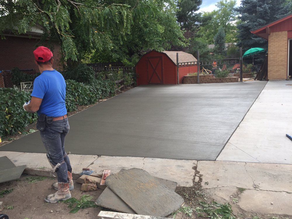 Fresh concrete driveway beside a walkway, with a person in a blue shirt and red cap standing near the edge.