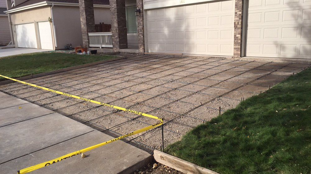 Driveway with textured concrete paving and yellow measuring tape in front of a garage and lawn.