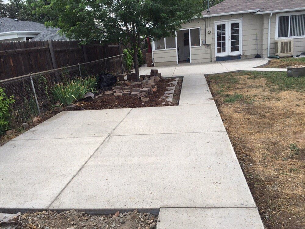Concrete backyard walkway leading to a house patio, with garden beds and a dry lawn on either side