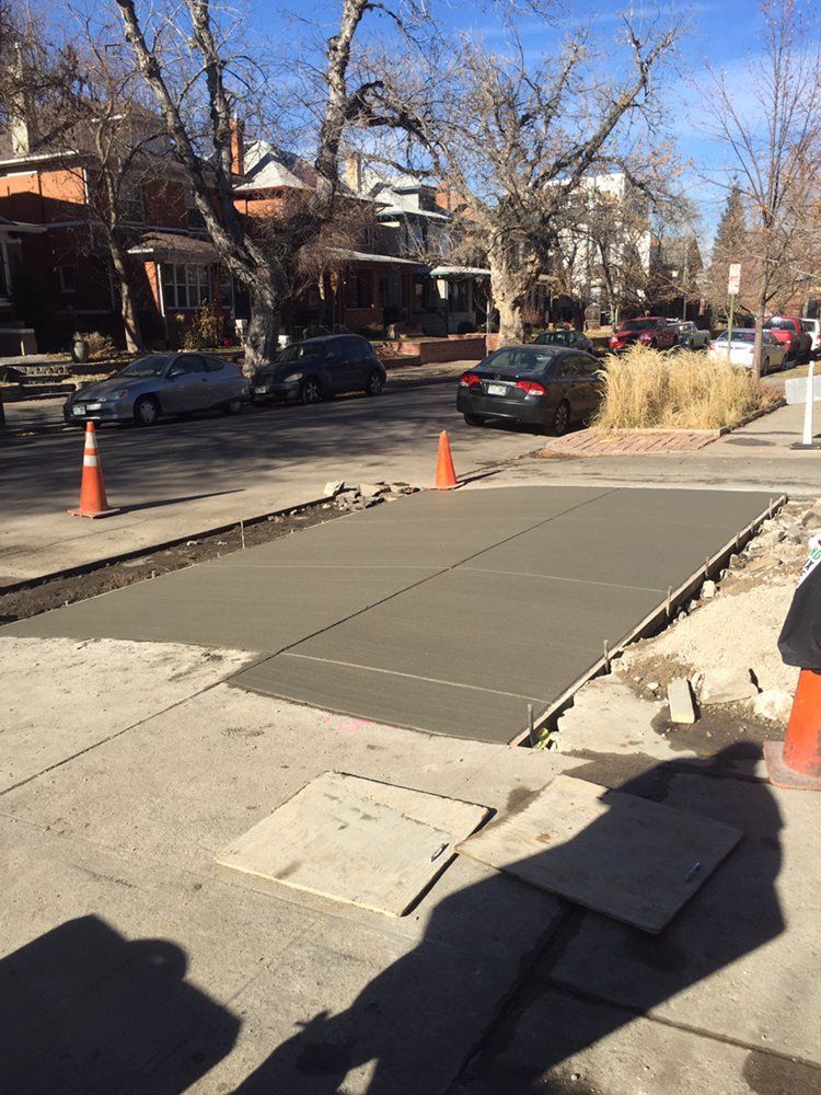 Street sidewalk ramp under construction with orange cones and parked cars on a residential street