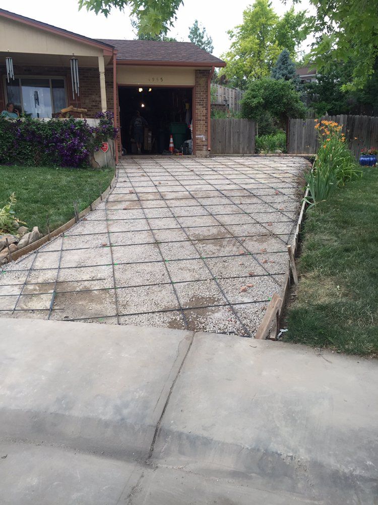Driveway leading to a house garage, with a cracked concrete surface and a tiled section in the center.