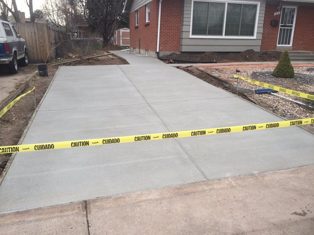 Fresh concrete driveway by a brick house, cordoned off with yellow caution tape.