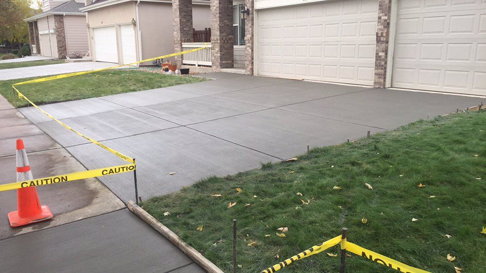 Cordoned-off driveway with wet concrete, orange cone, and caution tape in front of a garage.