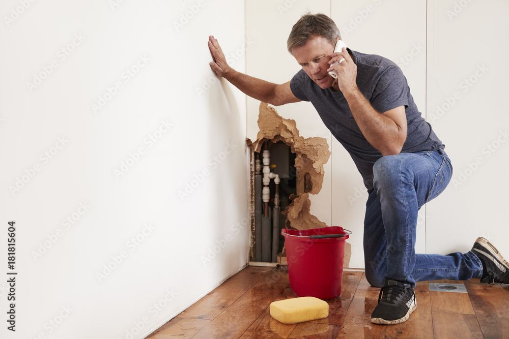 a man is kneeling down in front of a hole in the wall while talking on a cell phone .
