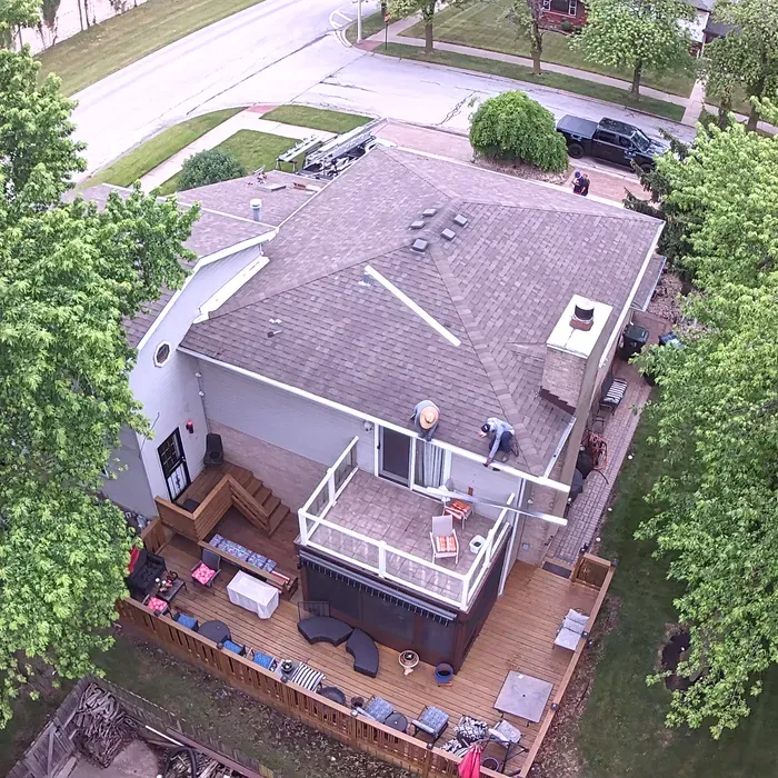 Aerial view of a house with a deck, a hot tub, and two people working on the roof.