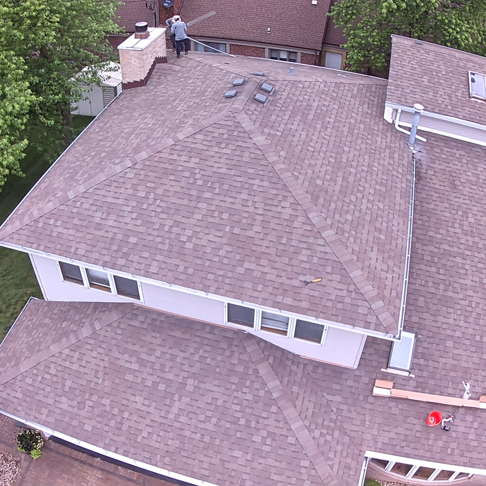 Overhead view of a house roof with shingles, a chimney, and a worker on the roof.