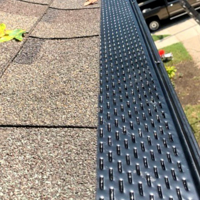 Gutter guard on roof edge with brown shingles. Gutter is black.