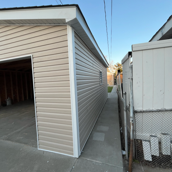Tan-sided garage with white trim next to a walkway and fence.