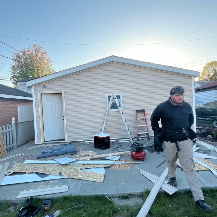 Man walking by a garage under construction; tools and materials are scattered on the concrete ground.