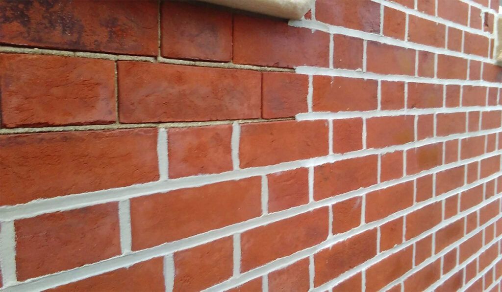Red brick wall with white mortar; partially damaged bricks at the top.