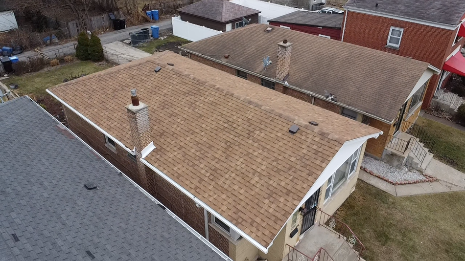 House roof with gray shingles, blue trim, and brick chimney against a blue sky with clouds.