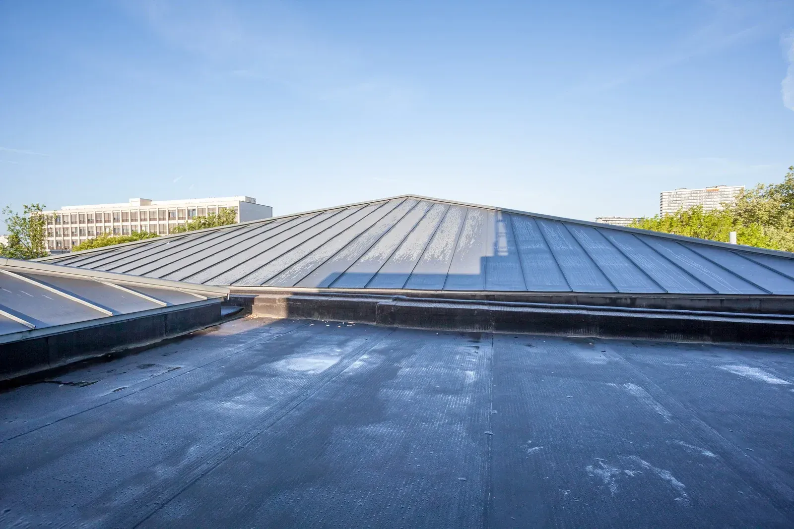 Flat black roof with a triangular, metal-clad roof section in the background, under a blue sky.