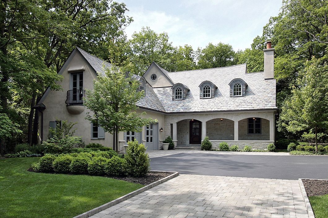 A large house with a driveway leading to it is surrounded by trees.