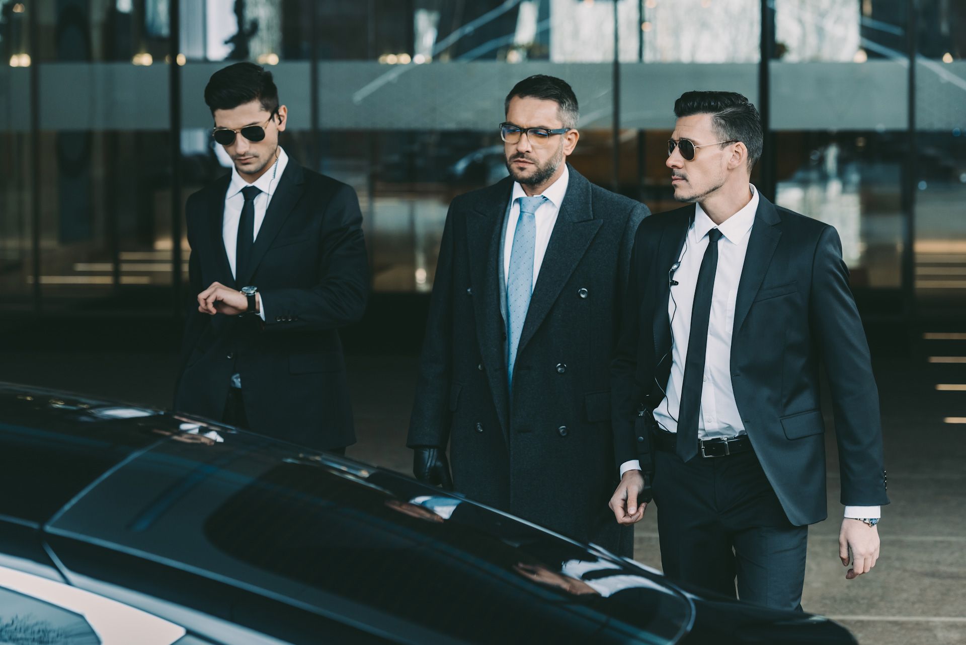Three men in suits and ties are standing next to a car.