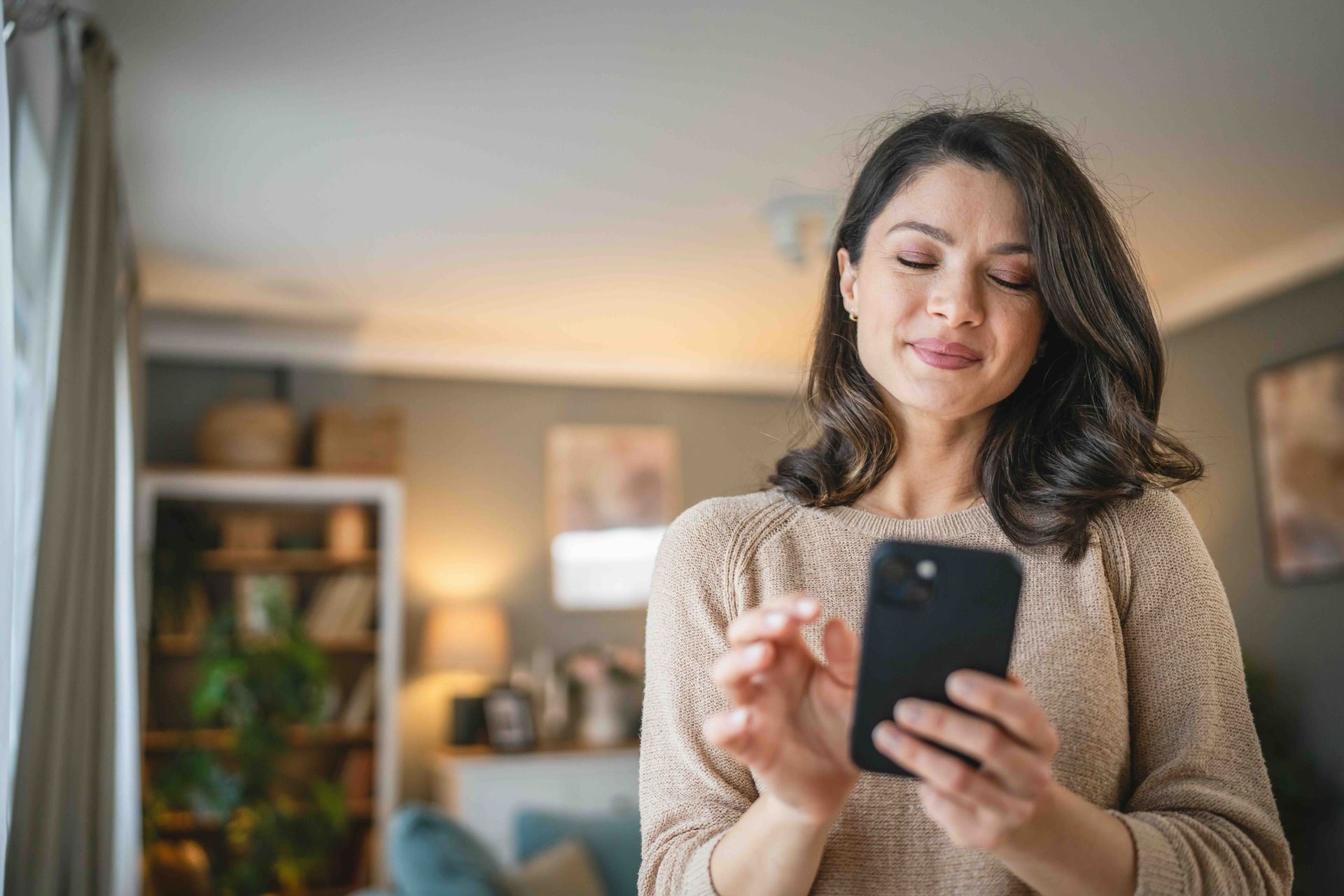 Woman smiling while using a smartphone in a cozy living room.