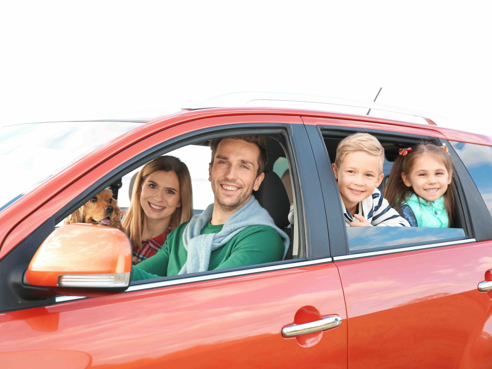 Family in an orange car, smiling. Two adults, two children. Bright, sunny setting.
