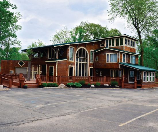 Wooden lodge-style building with multiple levels, large windows, and a surrounding deck.