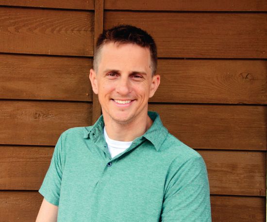 Man smiling in a green polo shirt and white undershirt, brown wooden background.
