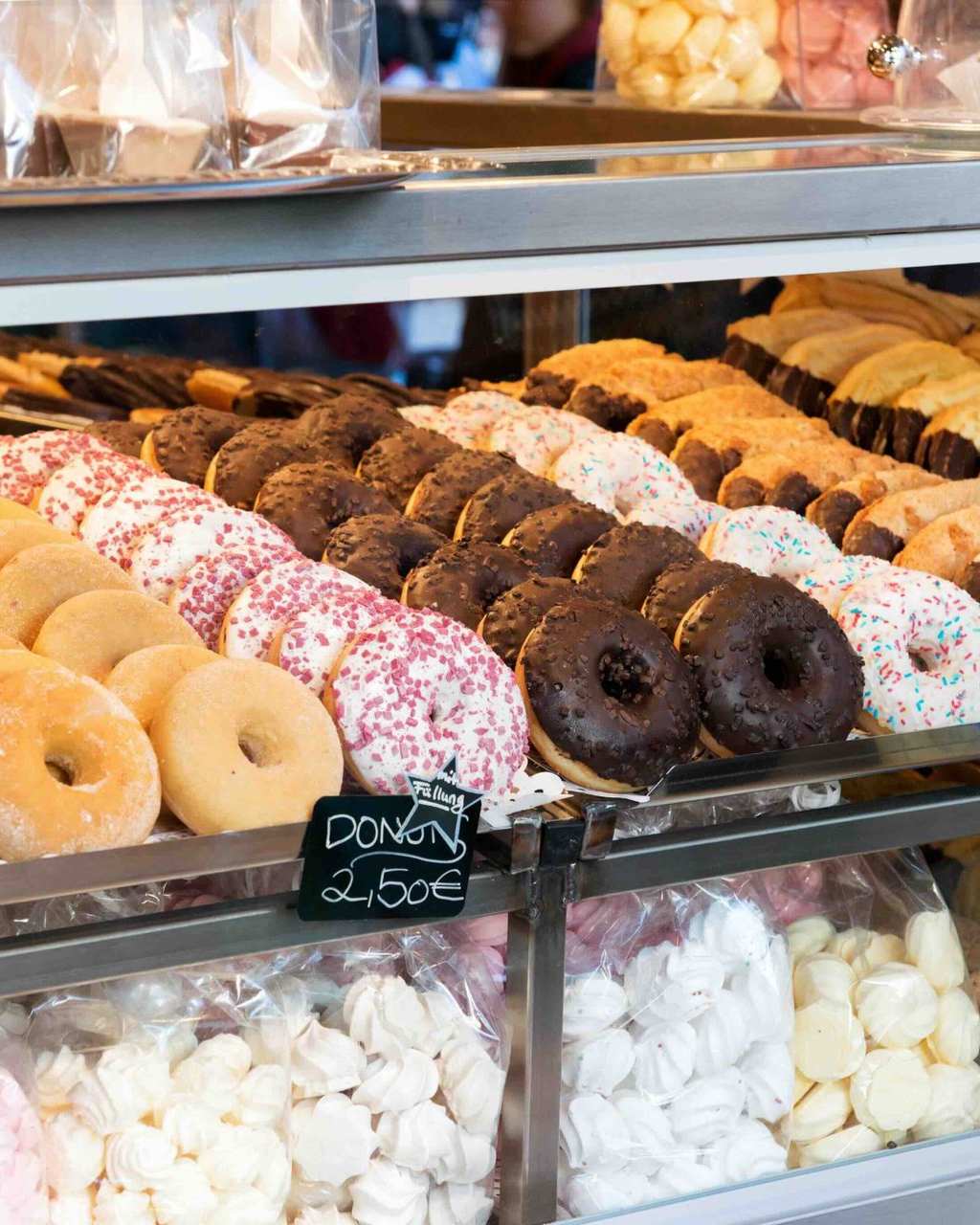 Display case filled with various donuts: glazed, chocolate, and sprinkled, in a bakery setting with price tag.