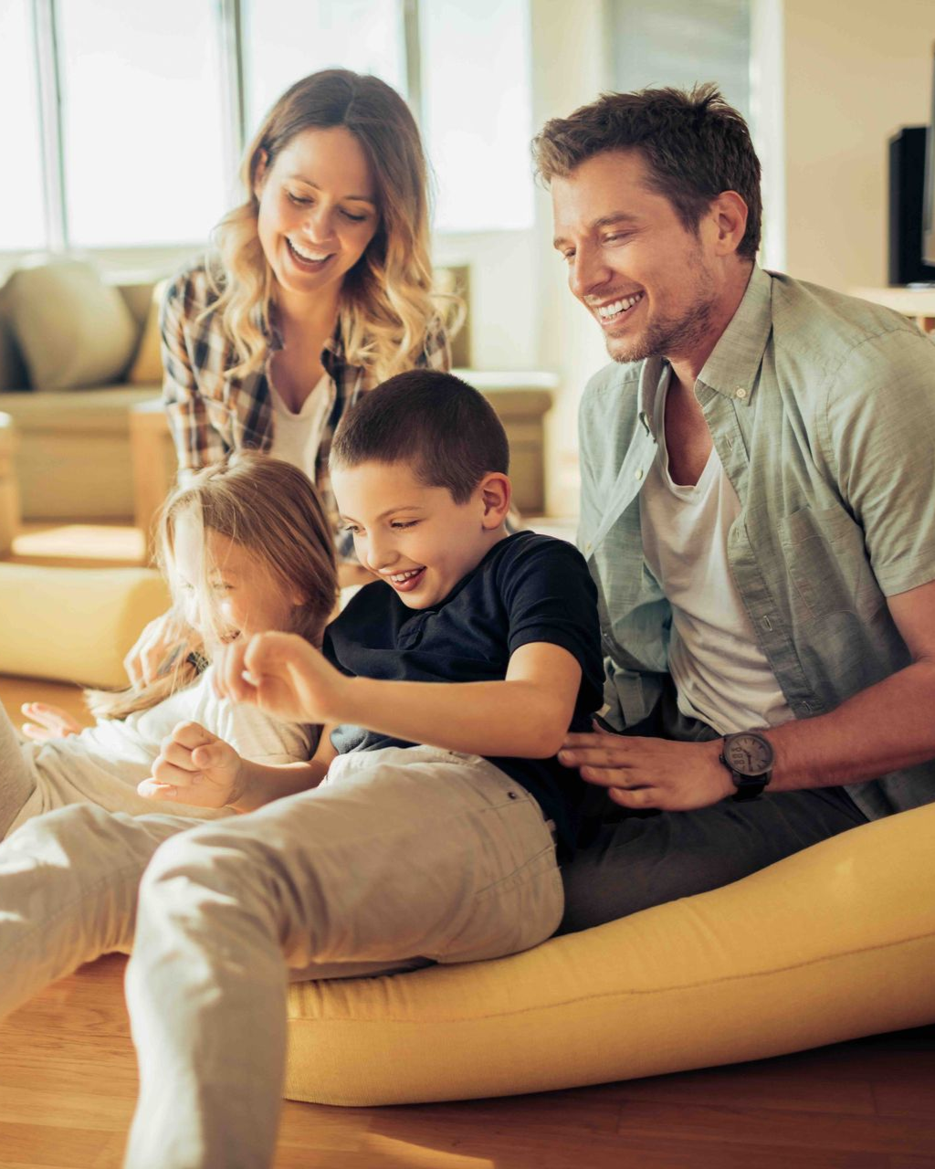 Family of four smiling and interacting on the floor of a living room.