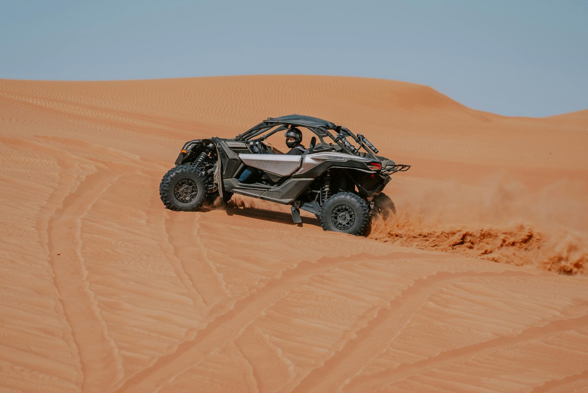 Off-road vehicle airborne over a dirt path, trees in the background.