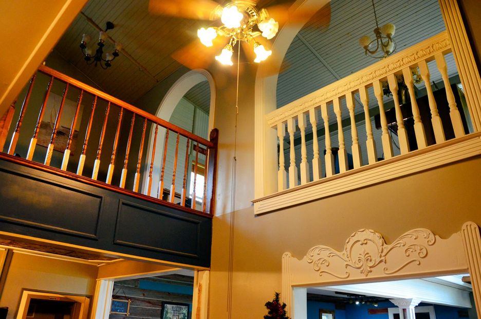 Interior view of a building with two mezzanine levels, brown and white railings, arched ceilings, and a ceiling fan.