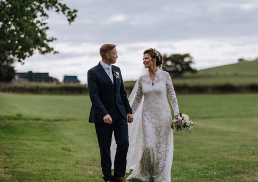 A bride and groom are walking in a field holding hands.