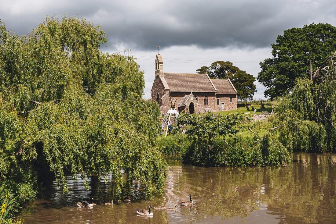 A small church is surrounded by trees and a body of water.