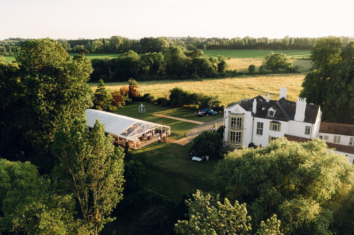 An aerial view of a large white house in the middle of a field surrounded by trees.