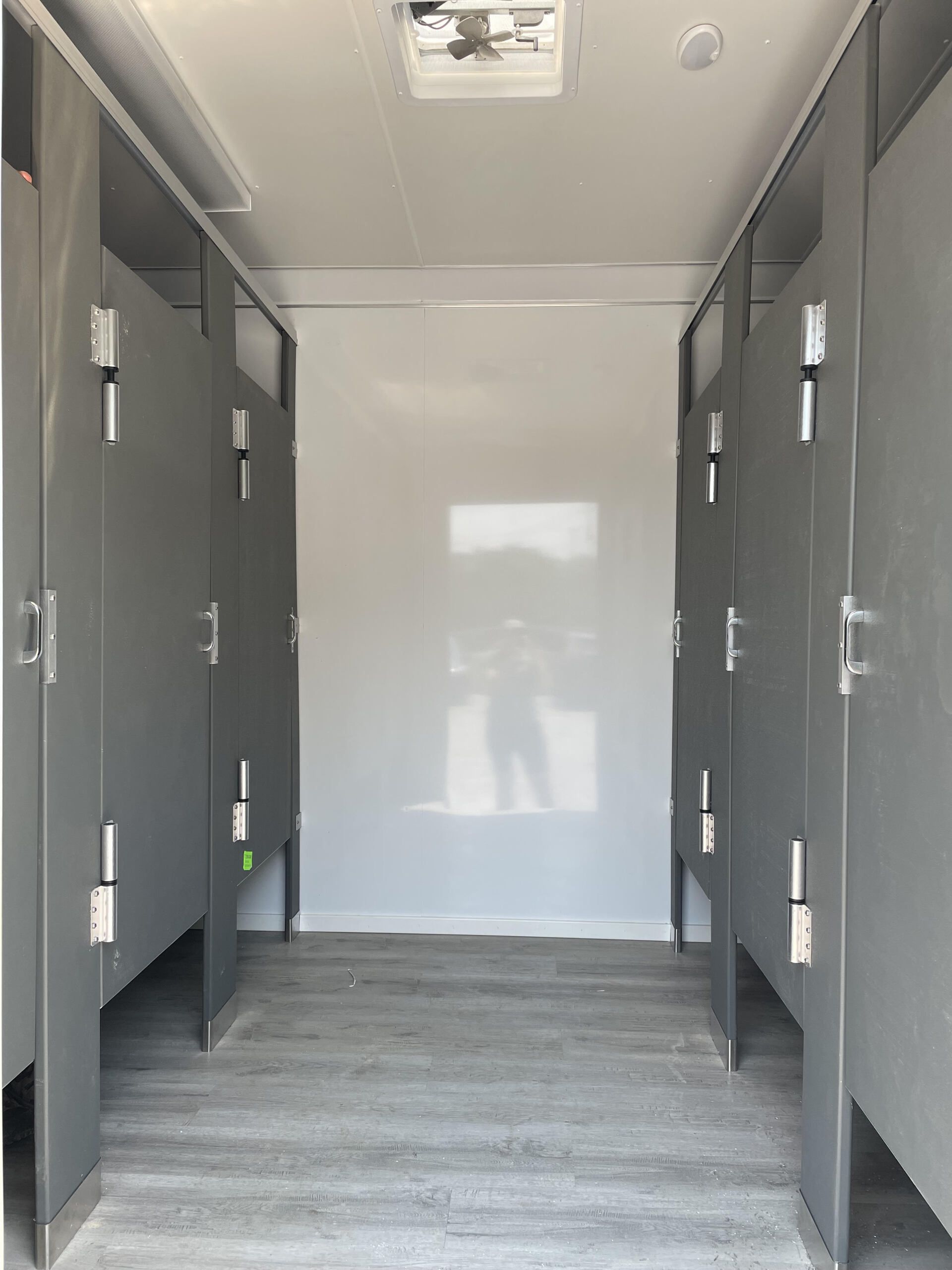 Interior of a gray restroom trailer with stall doors on both sides and a white back wall
