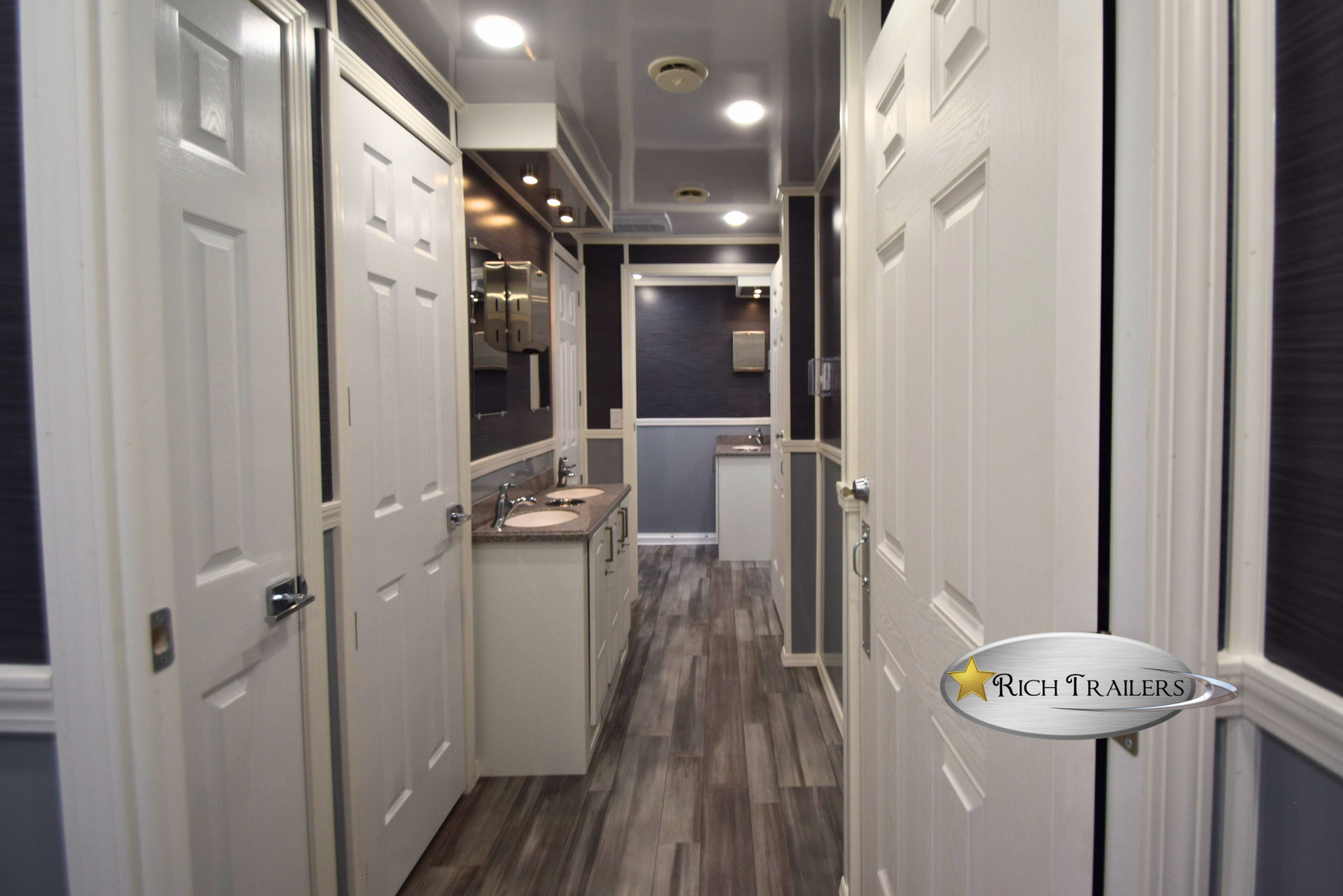 White portable restroom trailer with double doors and small windows, parked on gravel outdoors
