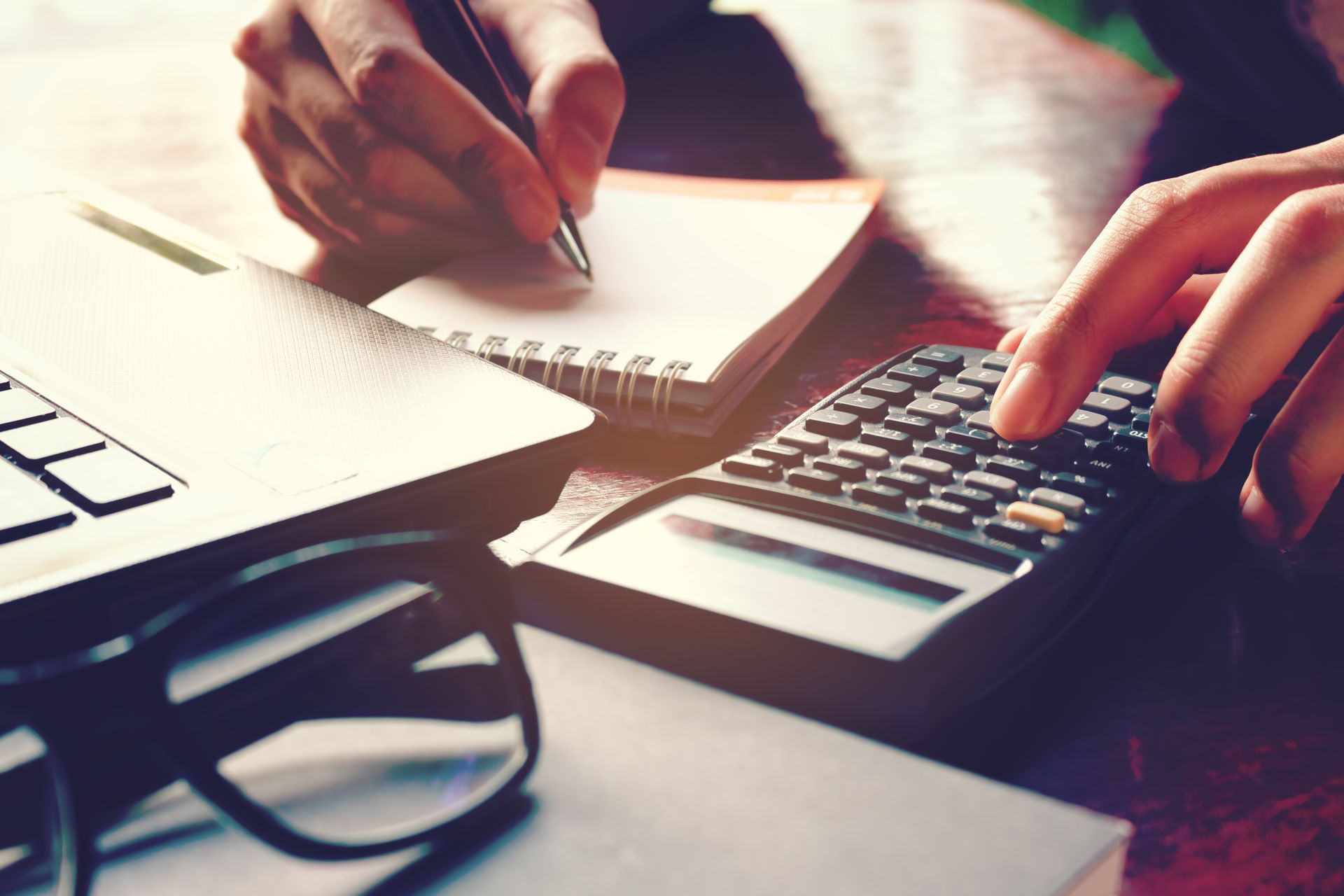 A person is writing in a notebook while using a calculator.