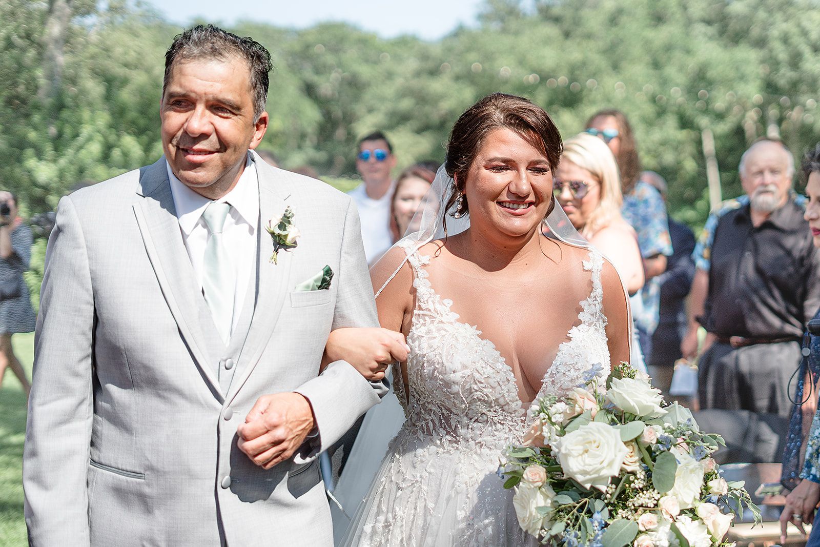 Bride and groom walking outdoors, smiling, with wedding guests in the background