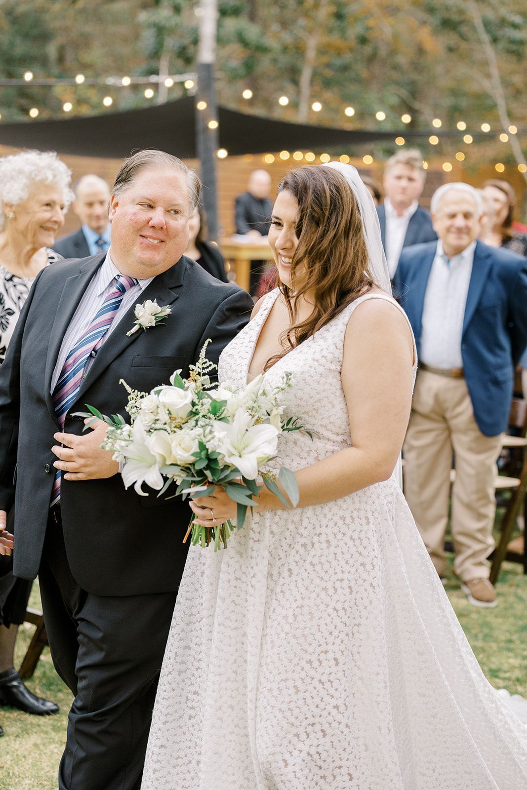 Bride and groom walking outdoors at a wedding reception, holding a bouquet and smiling