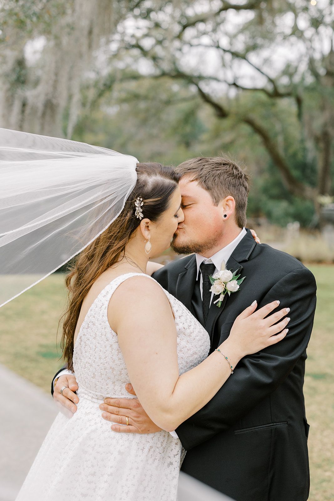 Bride and groom kissing under a flowing veil in an outdoor setting