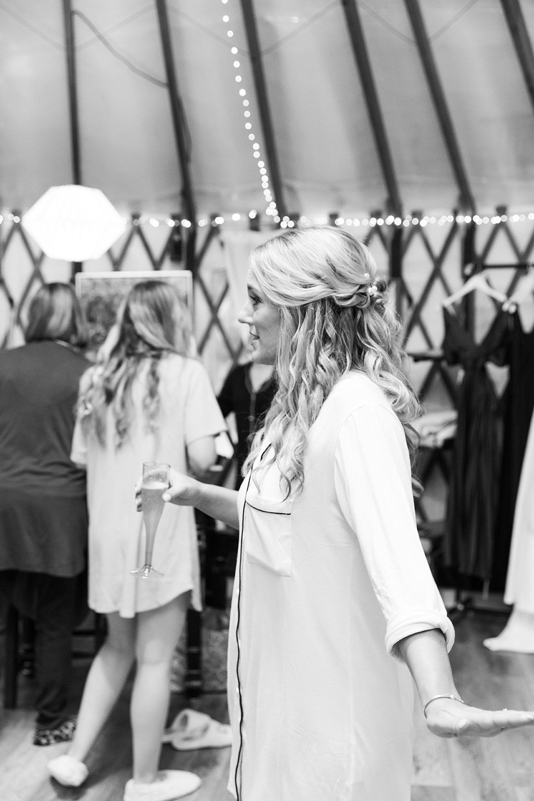 Woman with braided hair and floral headband holding a cup at a crowded outdoor event near a yurt-like tent