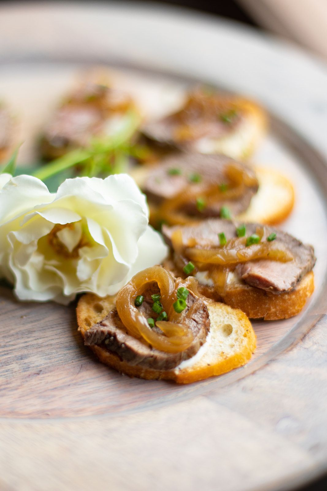 Mushroom crostini topped with herbs beside a white flower on a rustic plate