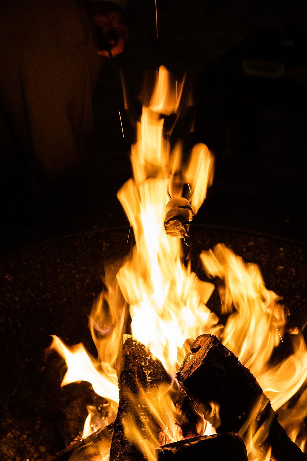 A bright campfire with tall orange flames burning logs in a dark outdoor setting