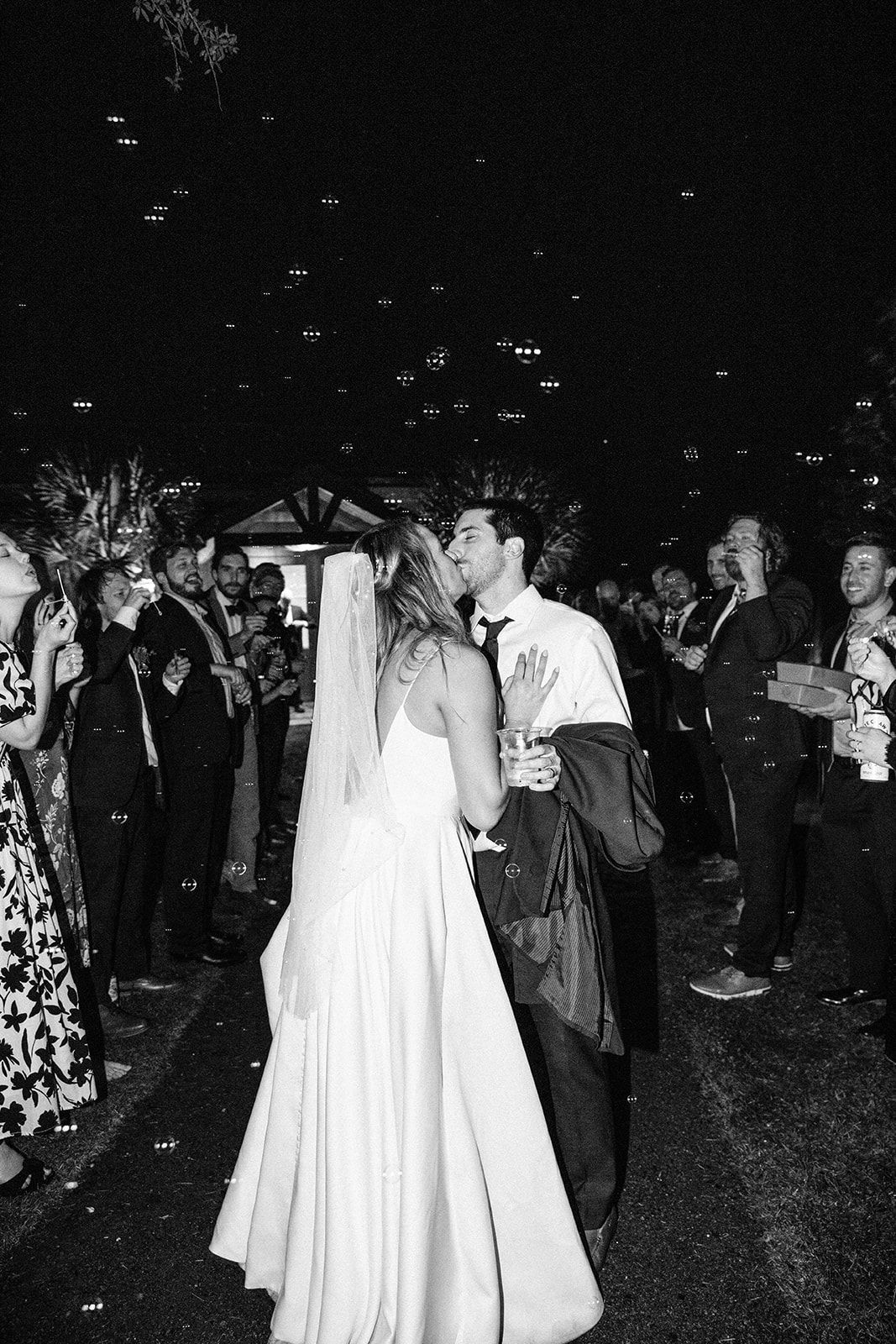 Bride and groom kissing at an outdoor wedding reception under falling confetti
