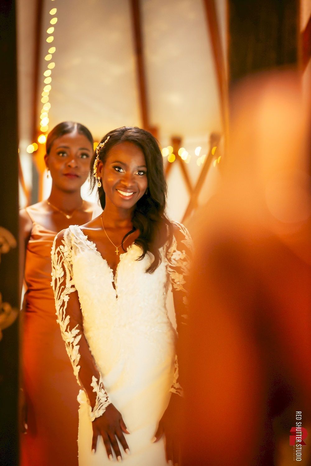 Two smiling people in white dresses standing in a warmly lit hallway with golden decor.