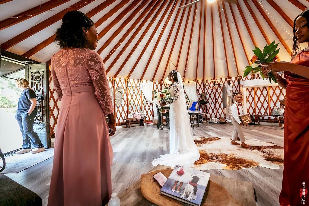 Bride in white stands in a decorated tent while a guest in a pink dress watches nearby.