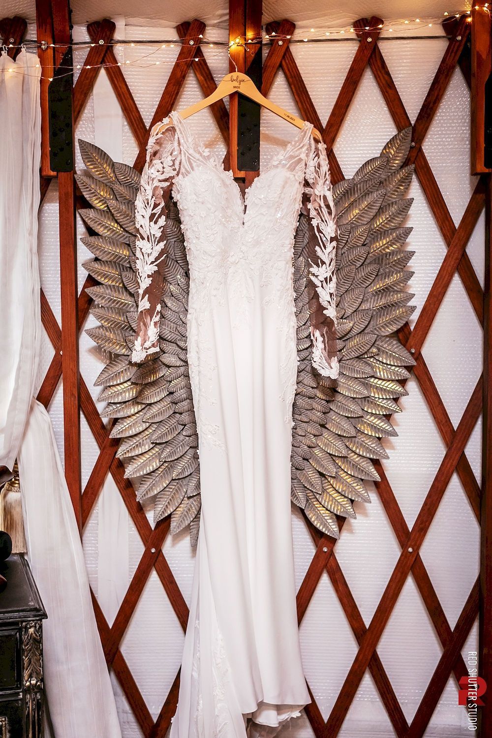 White dress with large silver feathered wings hanging on a wooden lattice wall.
