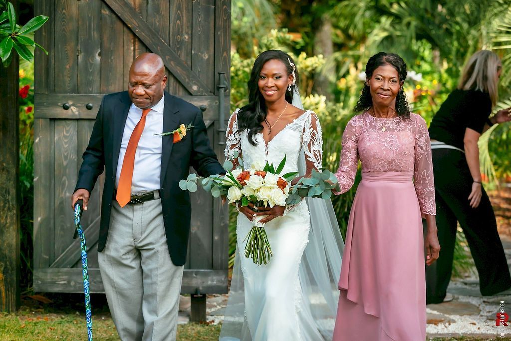 Wedding party walking outdoors in front of a rustic wooden doorway, bride in white with two attendants in pink dresses