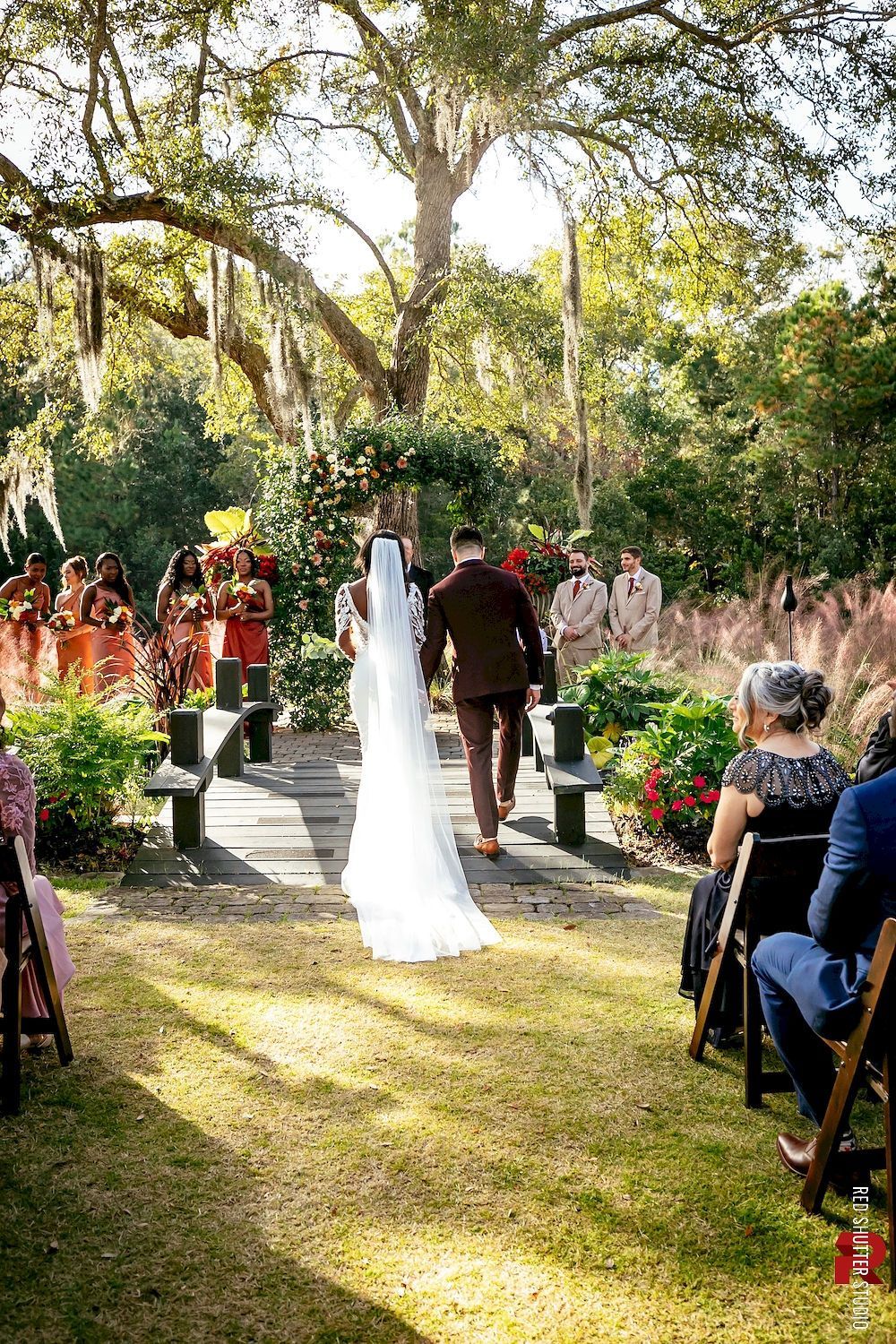 Bride and groom walking down a garden aisle at an outdoor wedding ceremony