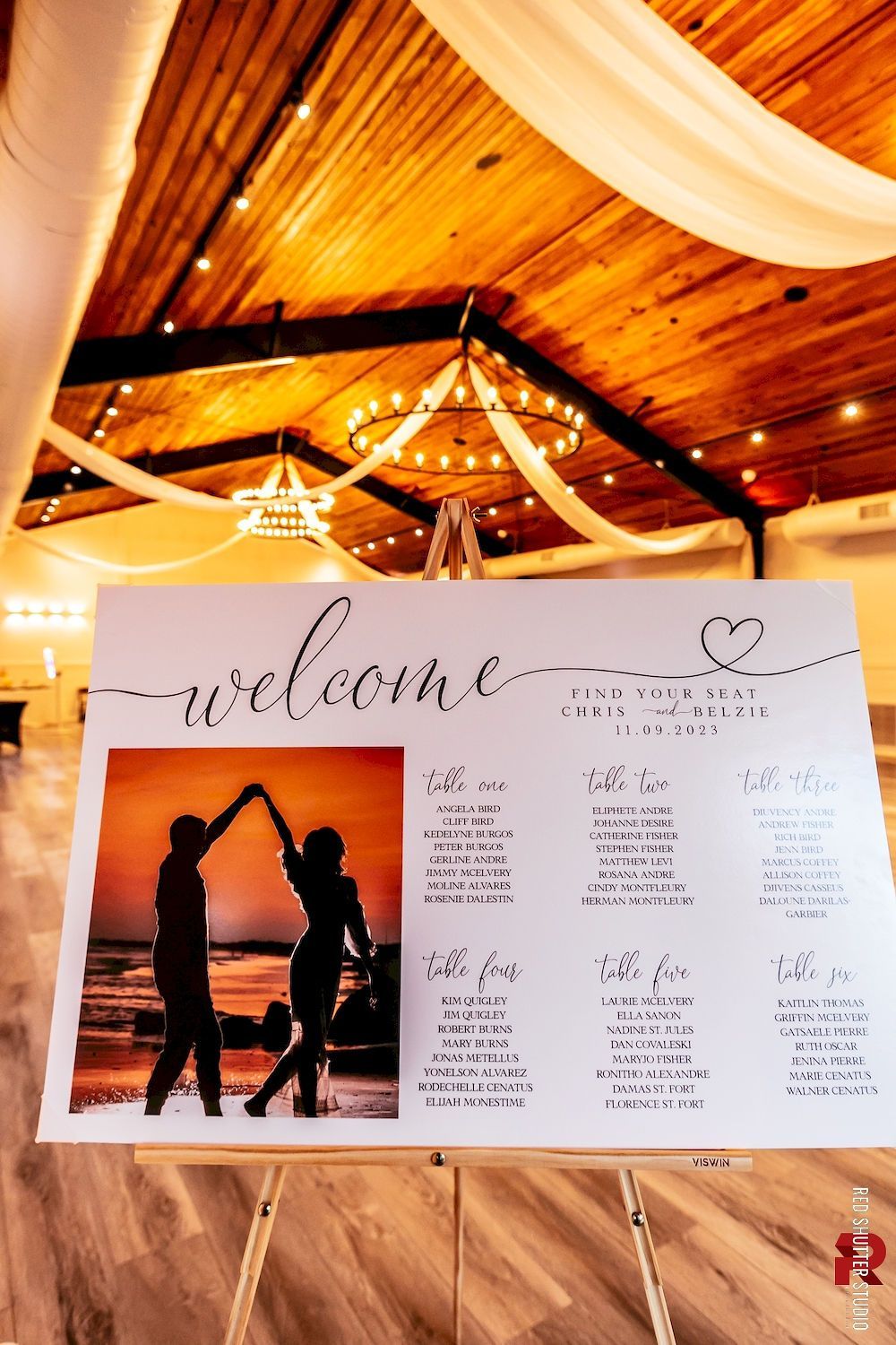 Wedding welcome sign on an easel under a wooden canopy, with a sunset couple silhouette and heart decorations