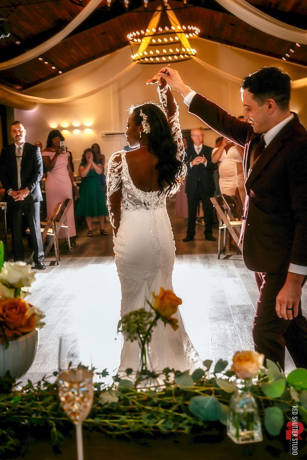 Wedding couple dancing under a tent, with guests watching and warm lights overhead.