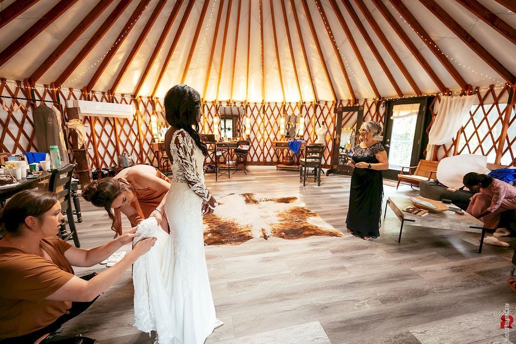 Inside a striped yurt, a woman in a white dress stands while others sit at tables in a warm, rustic setting