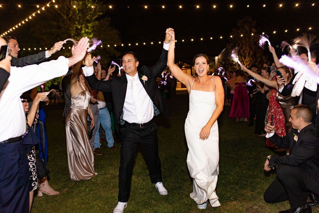 Newlyweds dancing with guests outdoors under string lights at a nighttime celebration